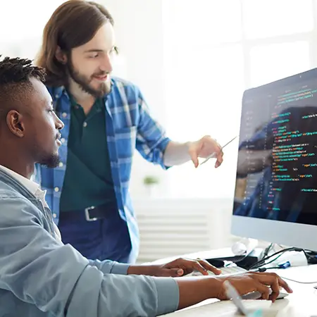 Two people look together at a desktop computer screen filled with lines of code.