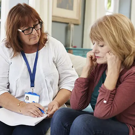 A human services worker takes notes while giving care to a distressed woman.